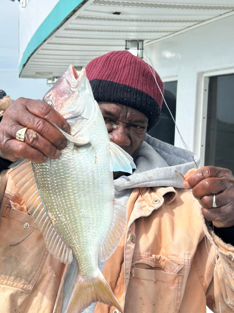 Person holding a fish on a boat, wearing a red beanie and beige jacket.