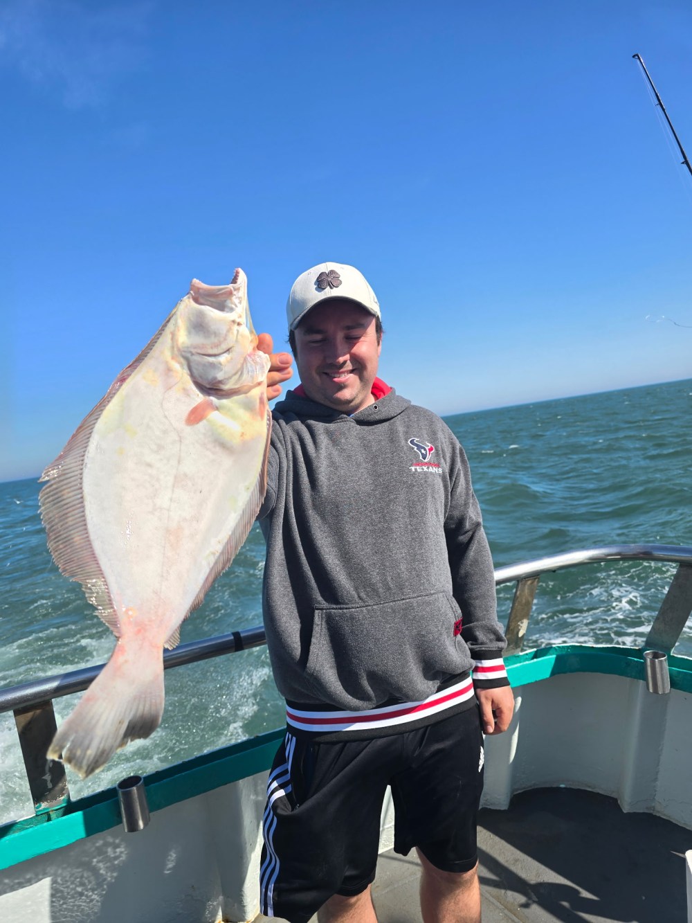 Person on boat holding a large fish against a clear blue sky.
