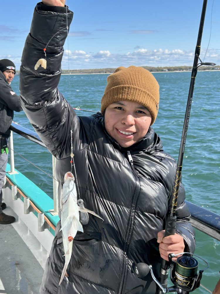 Person in puffer jacket and beanie holding a fishing rod with a fish on a boat.