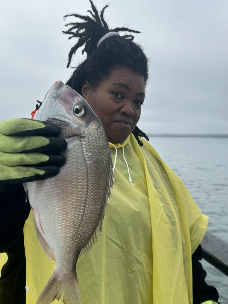 Person in yellow poncho holding a fish near water.