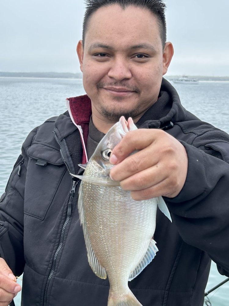 Person holding a fish while standing on a boat with water in the background.
