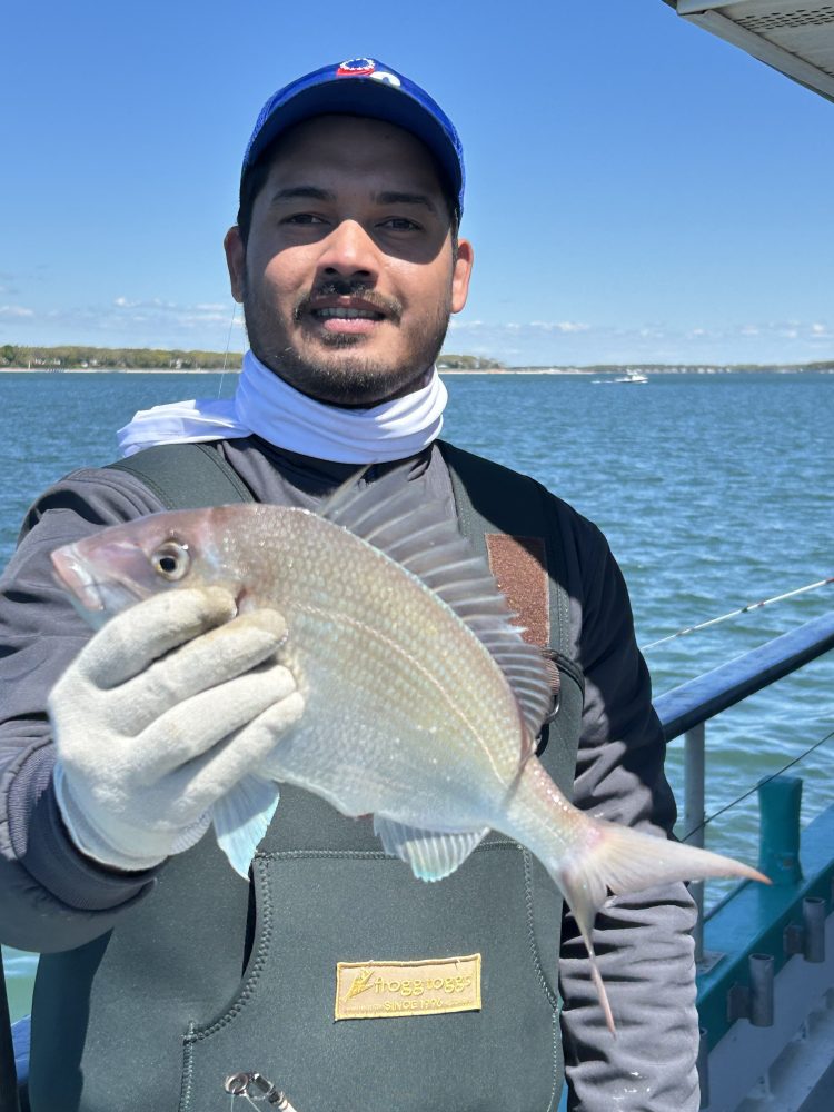 Man holding a fish on a boat with water in the background.