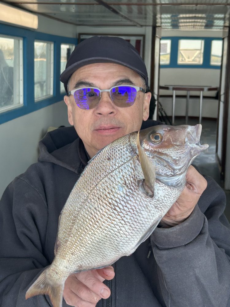 Person holding a large fish with both hands indoors, wearing sunglasses and a cap.