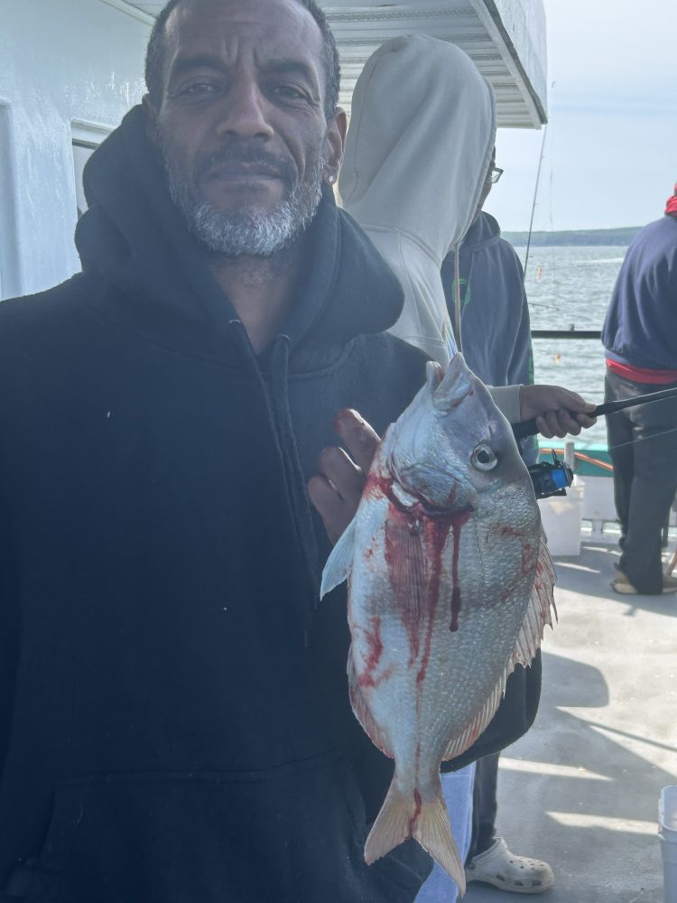 Person holding a large fish with visible red markings on a boat.