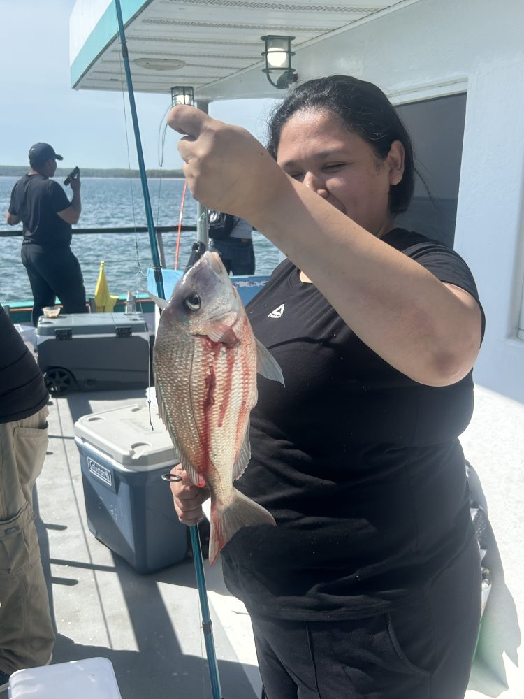 Person holding a caught fish on a boat, with water in background.