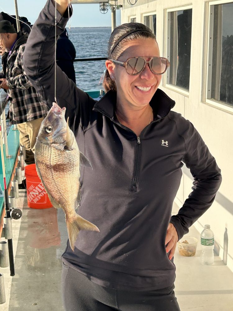Person smiling and holding a fish on a boat.