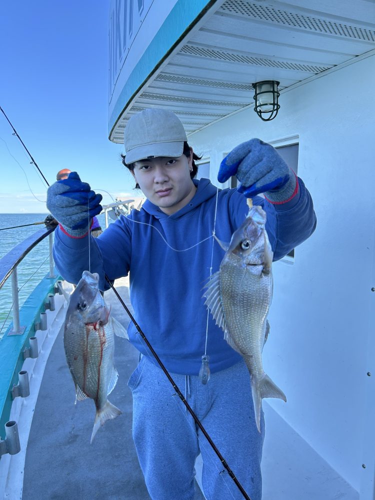Person on a boat holding two fish with fishing rods.