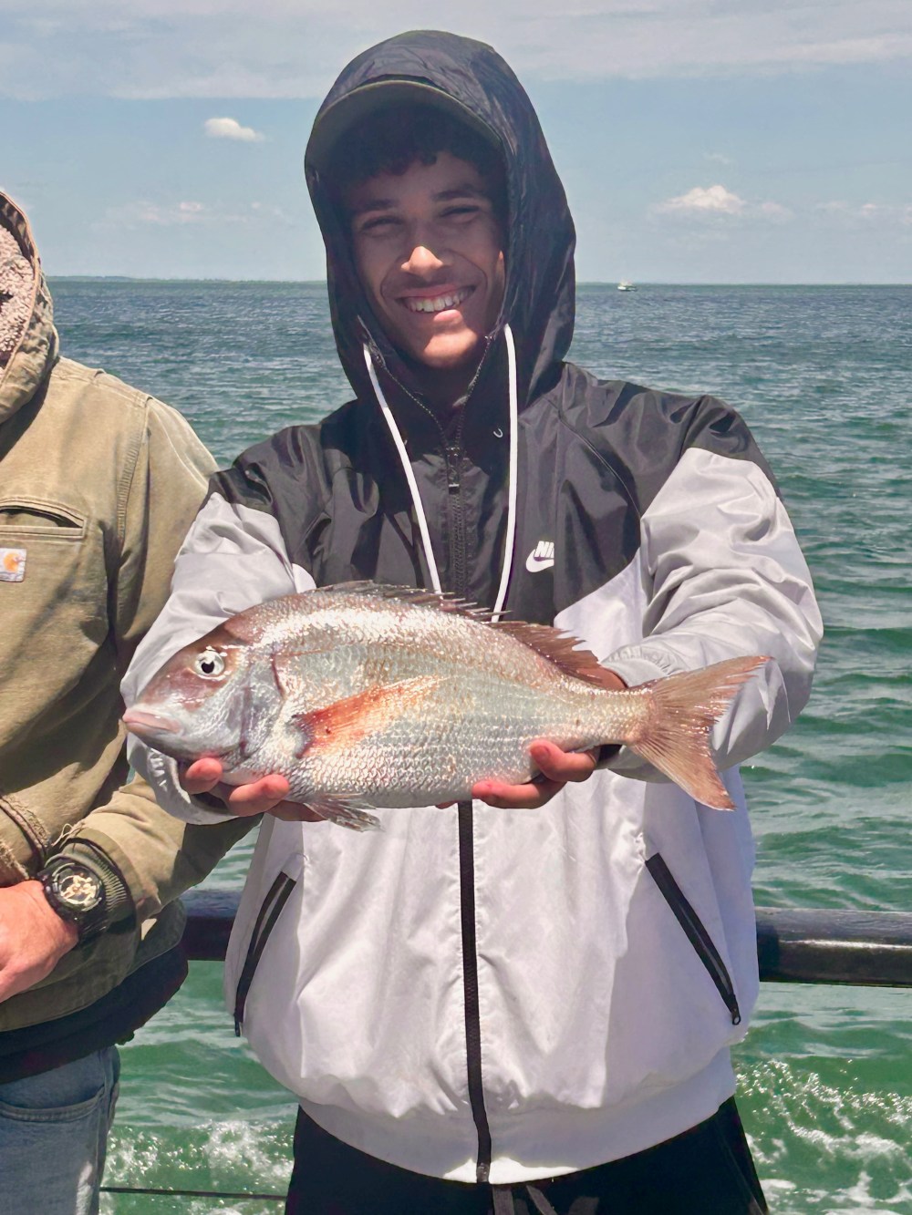 Person holding a fish, smiling on a boat with ocean backdrop.