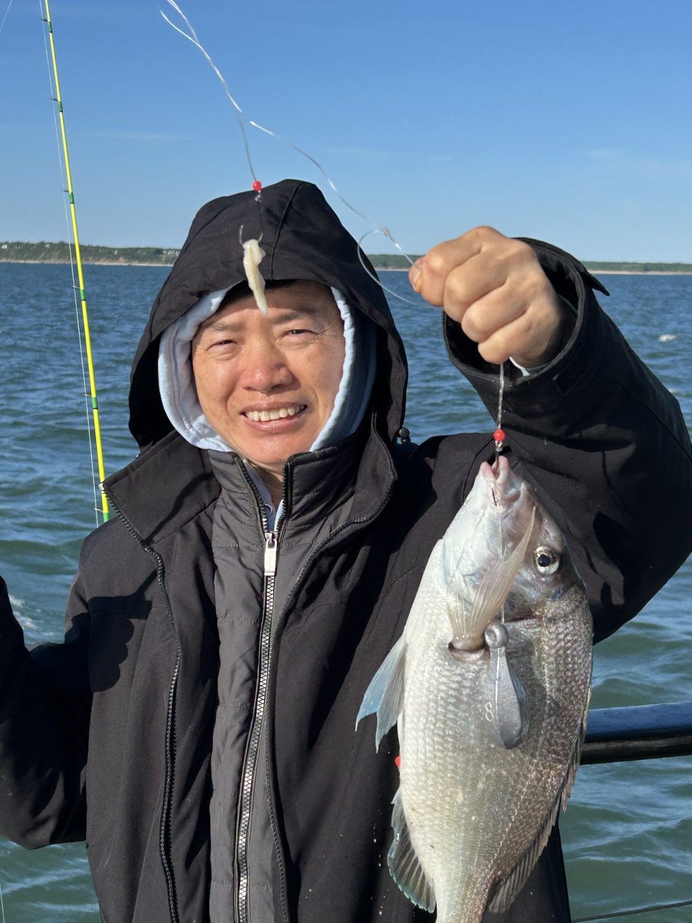 Person smiling as they hold a fish on a boat with water in the background.