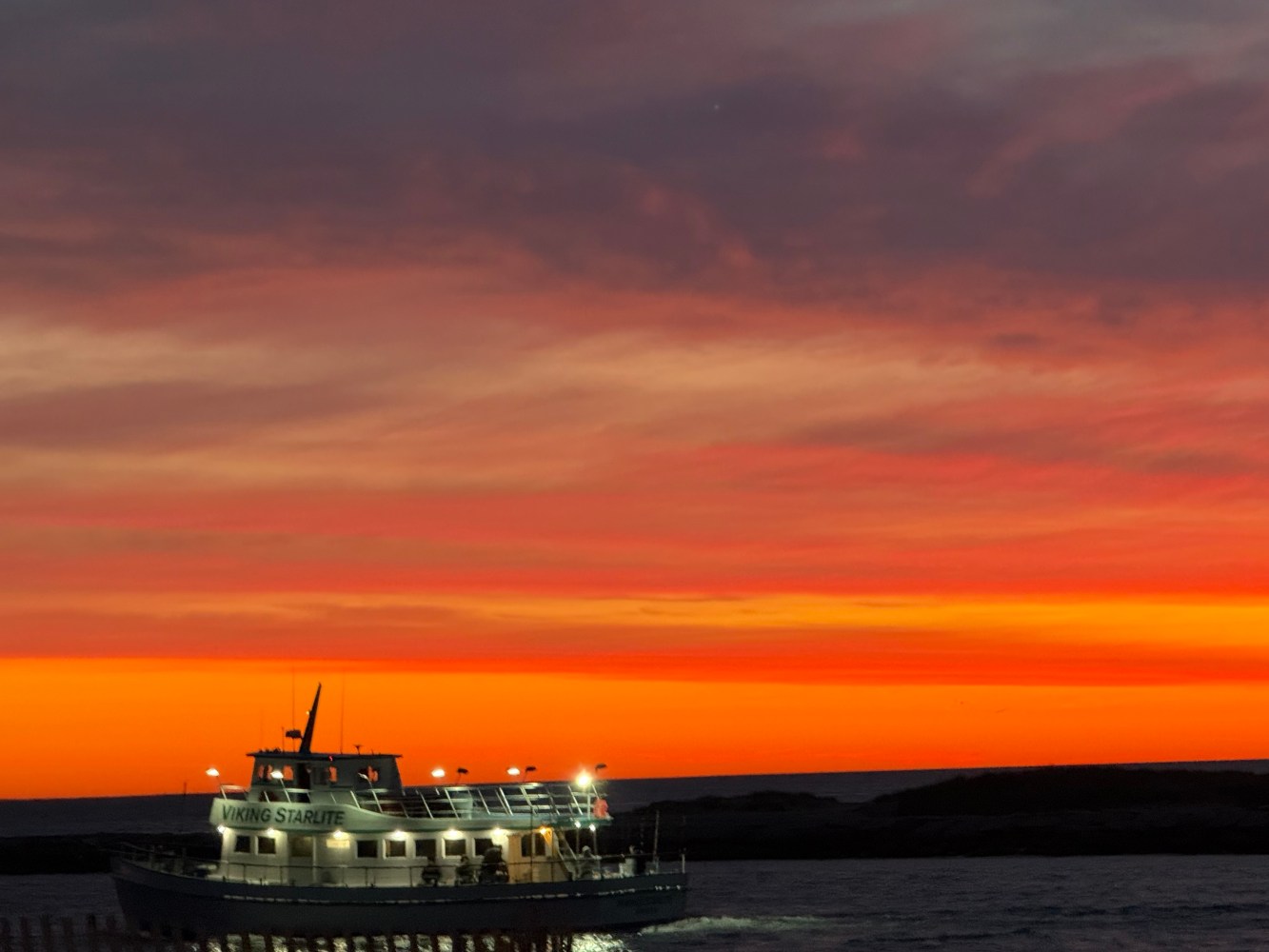 Boat on water during vibrant orange sunset with cloudy sky.