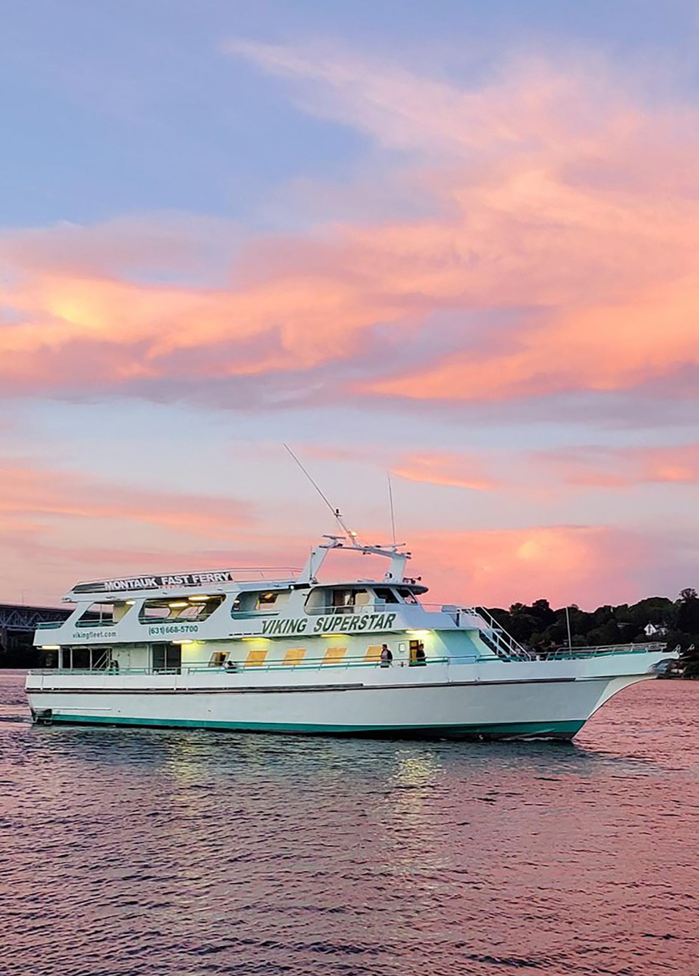 White yacht on water at sunset with pink clouds.