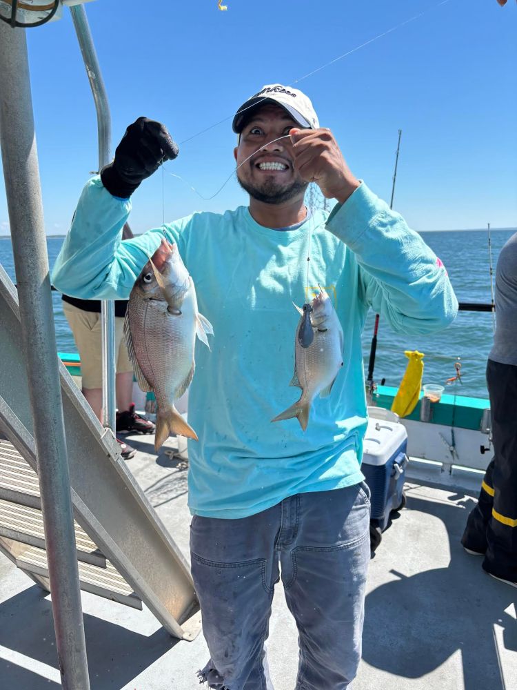 Man on boat holding two fish, one in each hand, smiling at the camera.