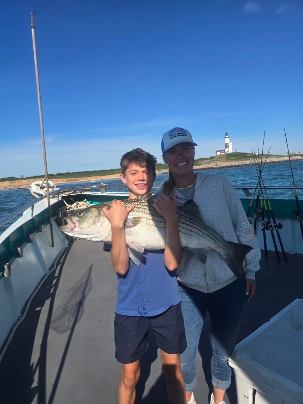 Kid holding large fish on boat with adult, lighthouse in background.