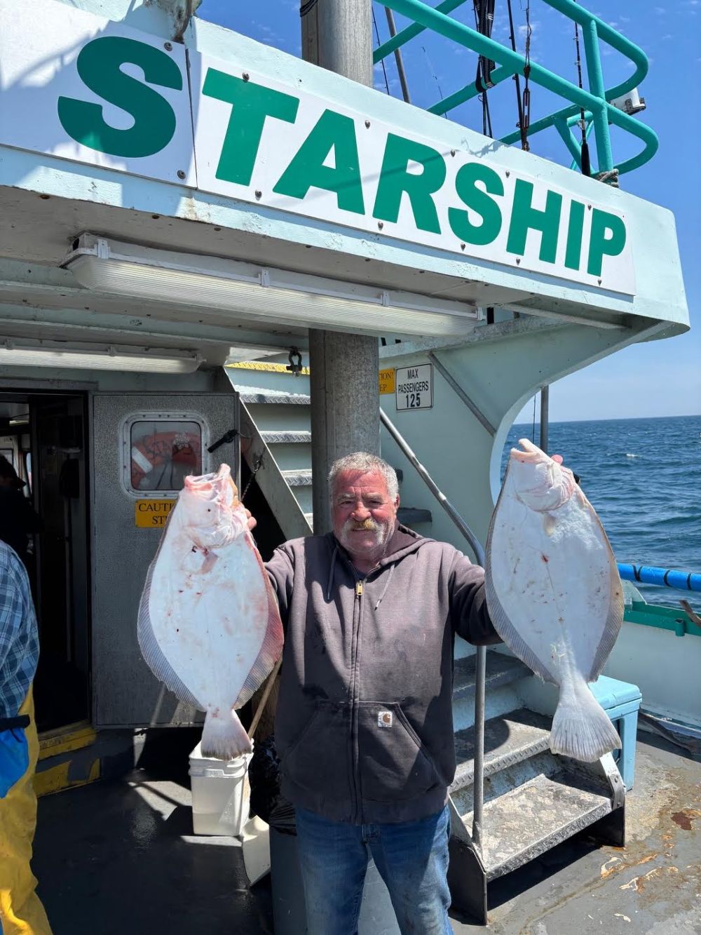 Man holding two large fish on a boat named Starship.