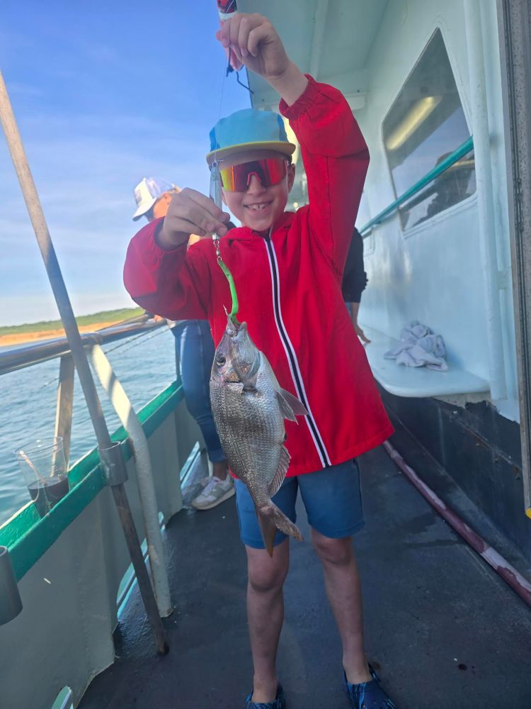 Child on boat holding a fish, wearing a red jacket and cap.