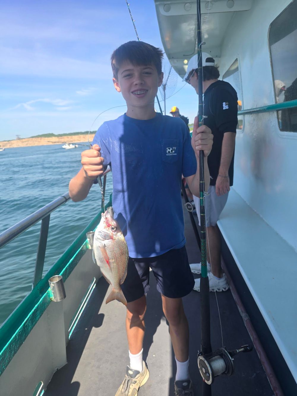 Boy on boat holding fishing rod and fish on a sunny day.