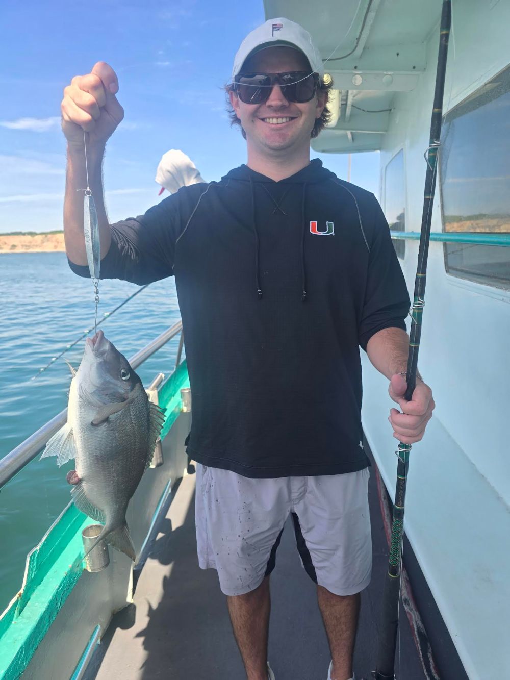Man on boat holding a caught fish and a fishing rod.