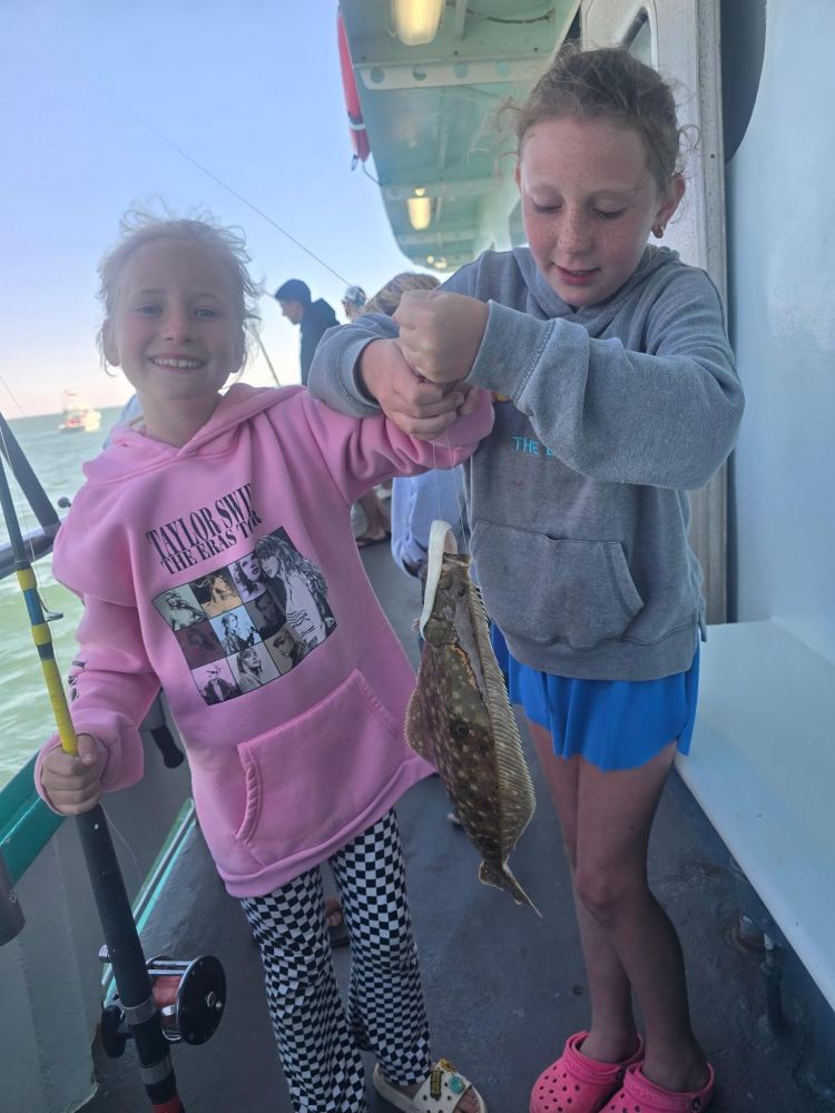Two children on a boat holding a fish, smiling.