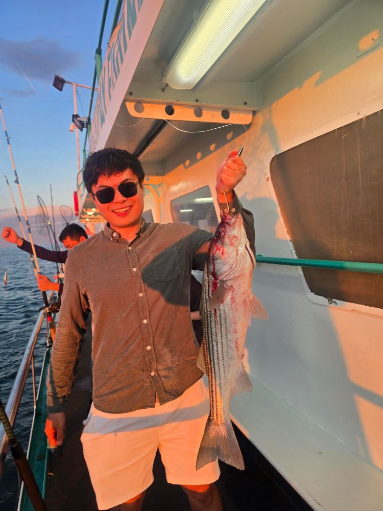 Man on boat holding a large fish, smiling in sunglasses and casual wear.