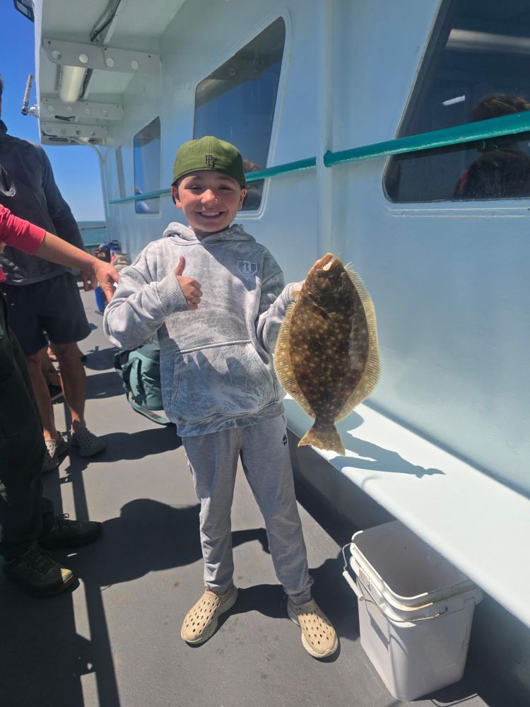 Child on boat holding a flat fish, smiling and giving a thumbs-up.