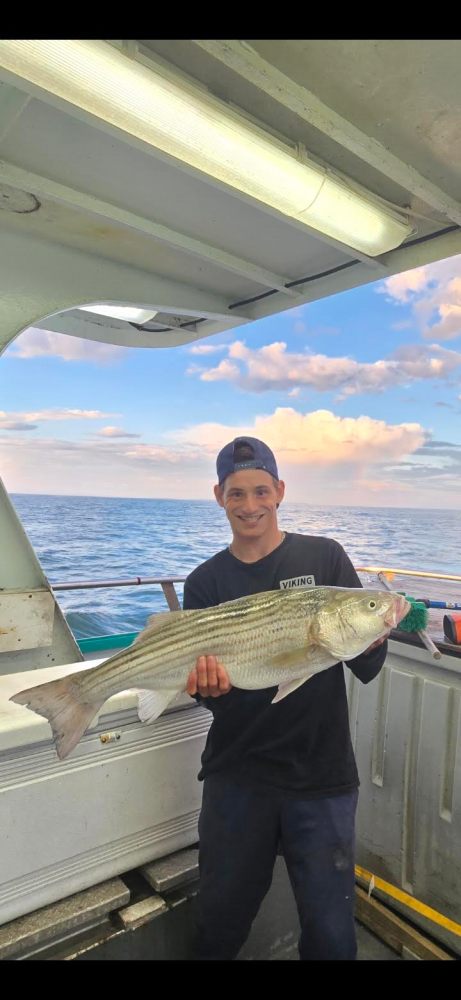 Person holding a large fish on a boat with ocean and clouds in the background.