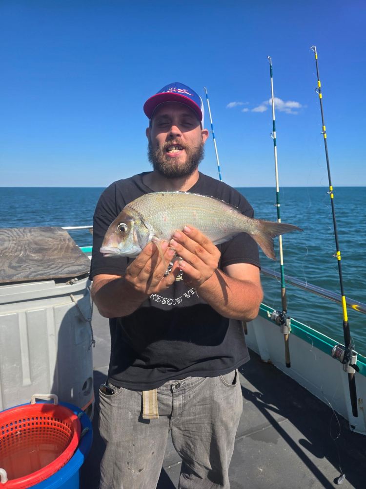 Man holding a fish on a boat with fishing rods in the background.