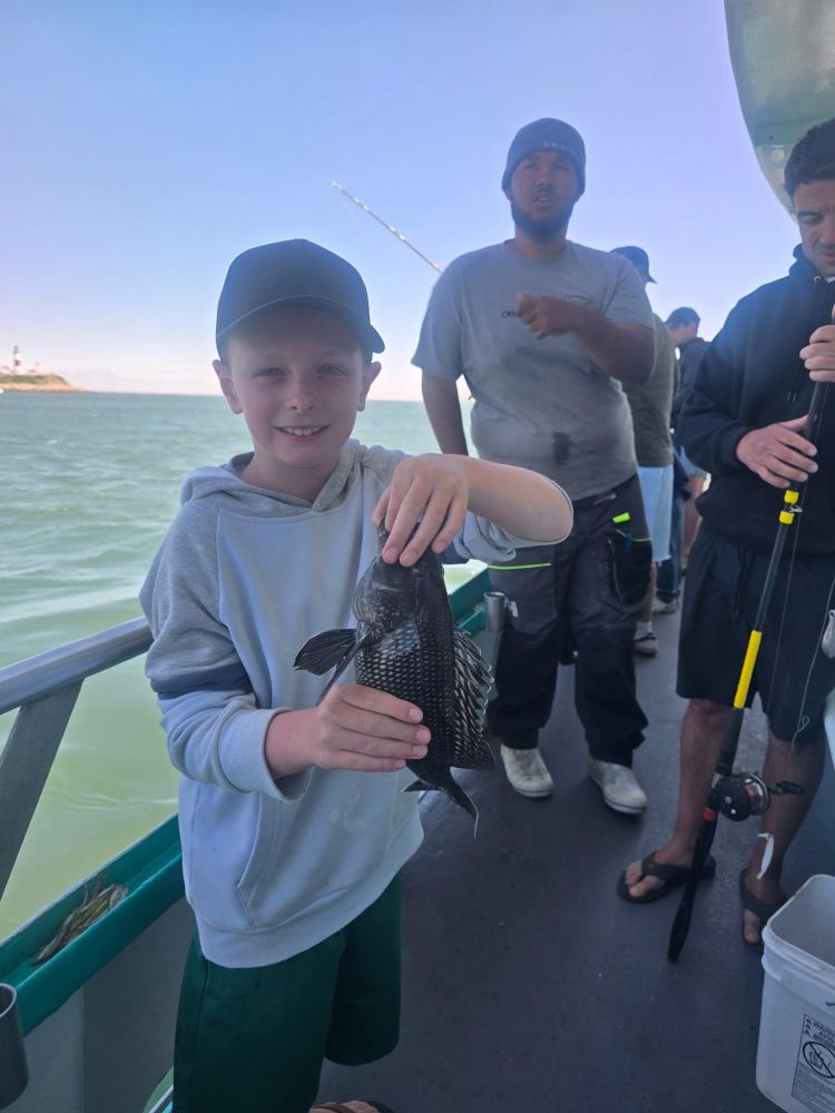 Boy holding fish on a boat with group of people around.
