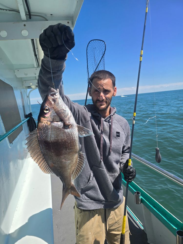 Man on boat holding a caught fish with fishing rod, ocean in the background.