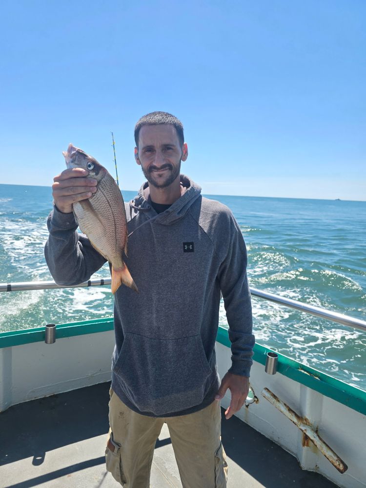 Person holding a fish on a boat with ocean in the background.