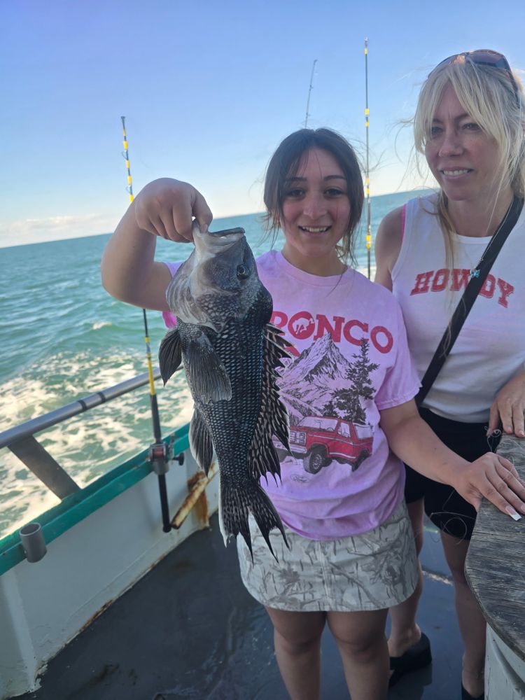 Two people on a boat holding a large fish with a blue ocean in the background.