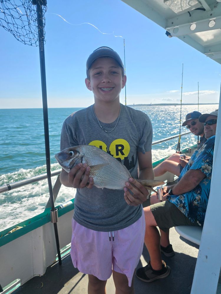 Person holding a fish on a boat with ocean in the background.