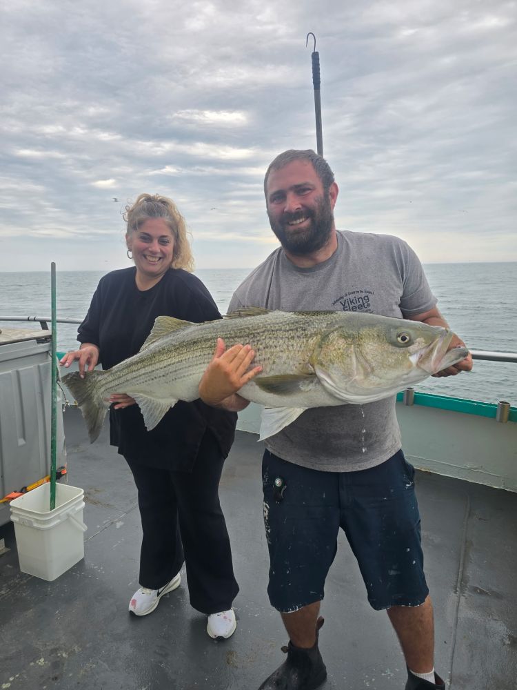 Two people on a boat holding a large fish together.