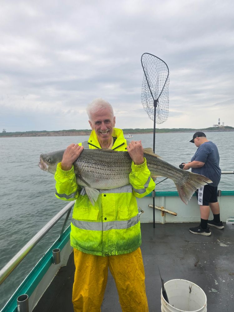 Man holding large fish on a boat, wearing yellow rain gear.