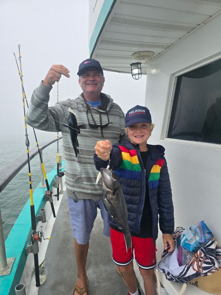 Two people on a boat proudly holding up their catch of fish.