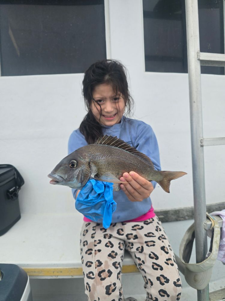 Child holding a fish on a boat, wearing leopard print pants and a blue top.