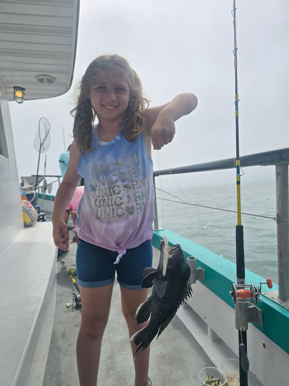 Child on a boat holding a fish, with fishing rod nearby.