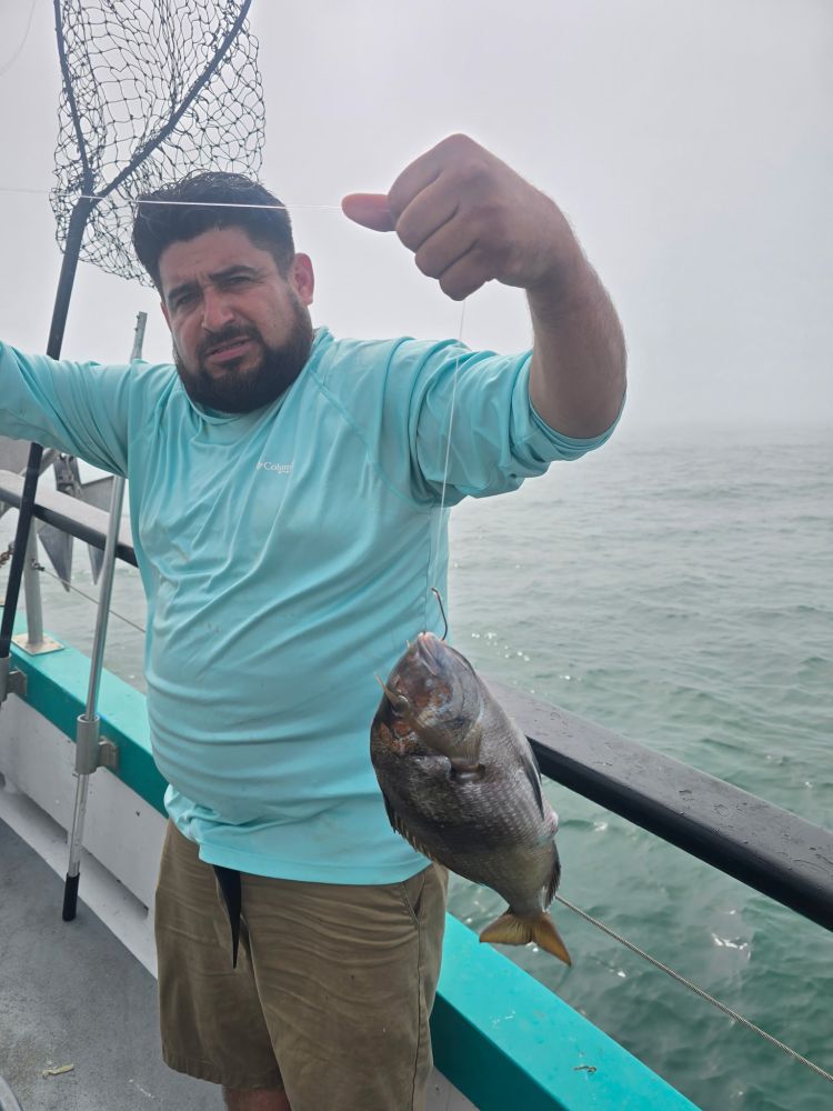 Man holding a fish on a boat, net in background.