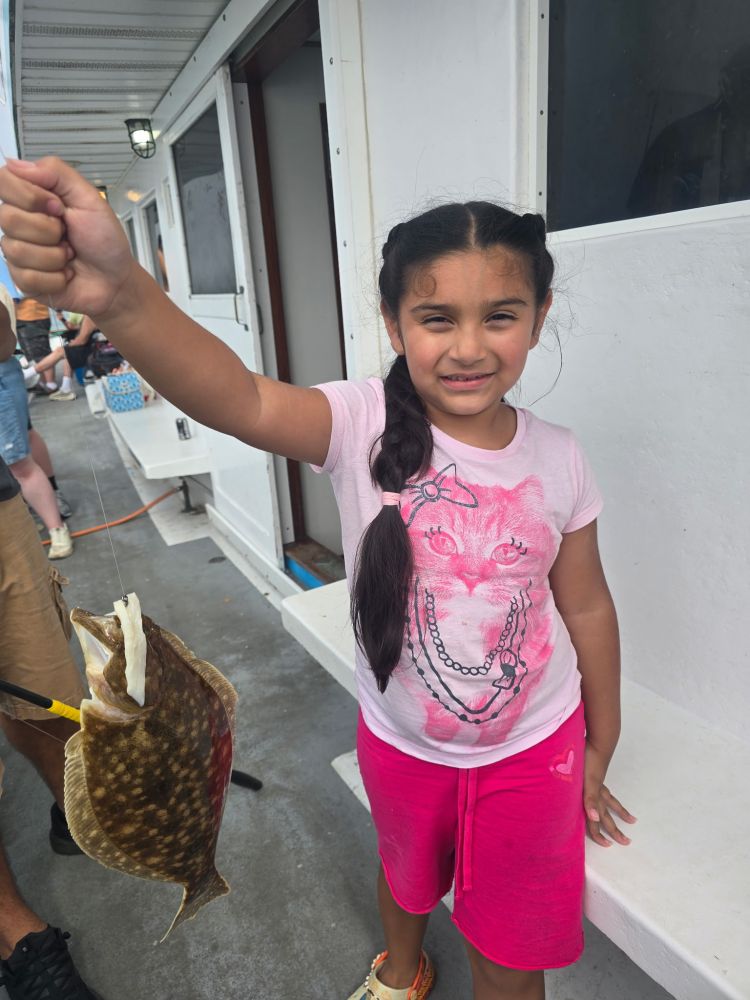 Girl holding a flat fish aboard a boat, smiling.