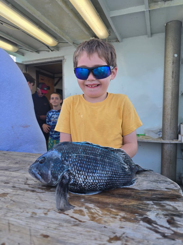 Child in yellow shirt with sunglasses holds a large fish on a boat.
