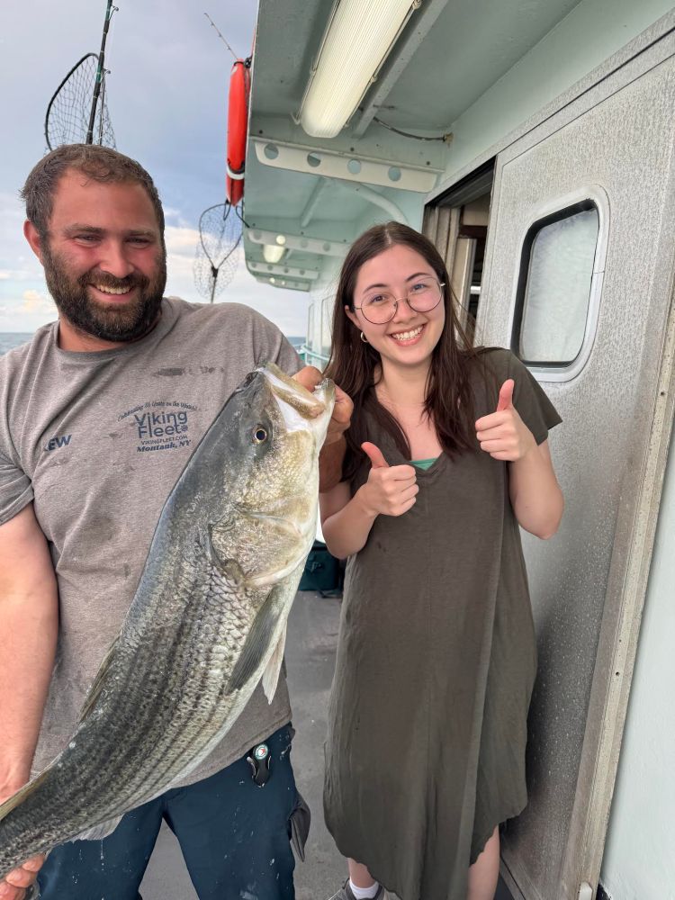 Man holding large fish next to smiling woman showing thumbs up on a boat.