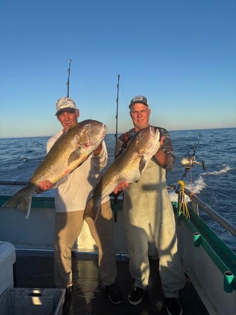 Two men on a boat holding large fish with ocean in background.