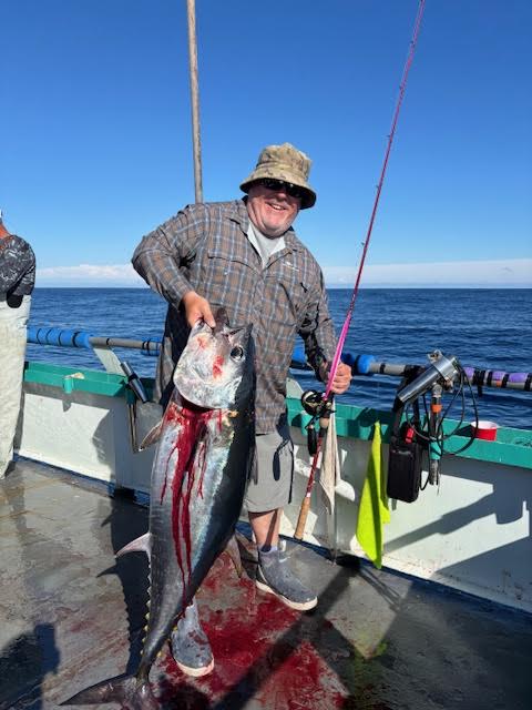 Man on boat holding a large fish next to fishing rod, ocean in background.