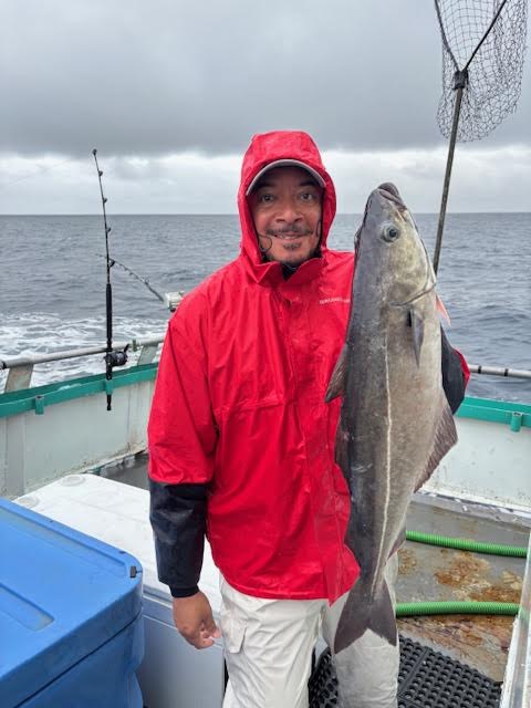 Person in red raincoat on boat holding a large fish, cloudy sky.