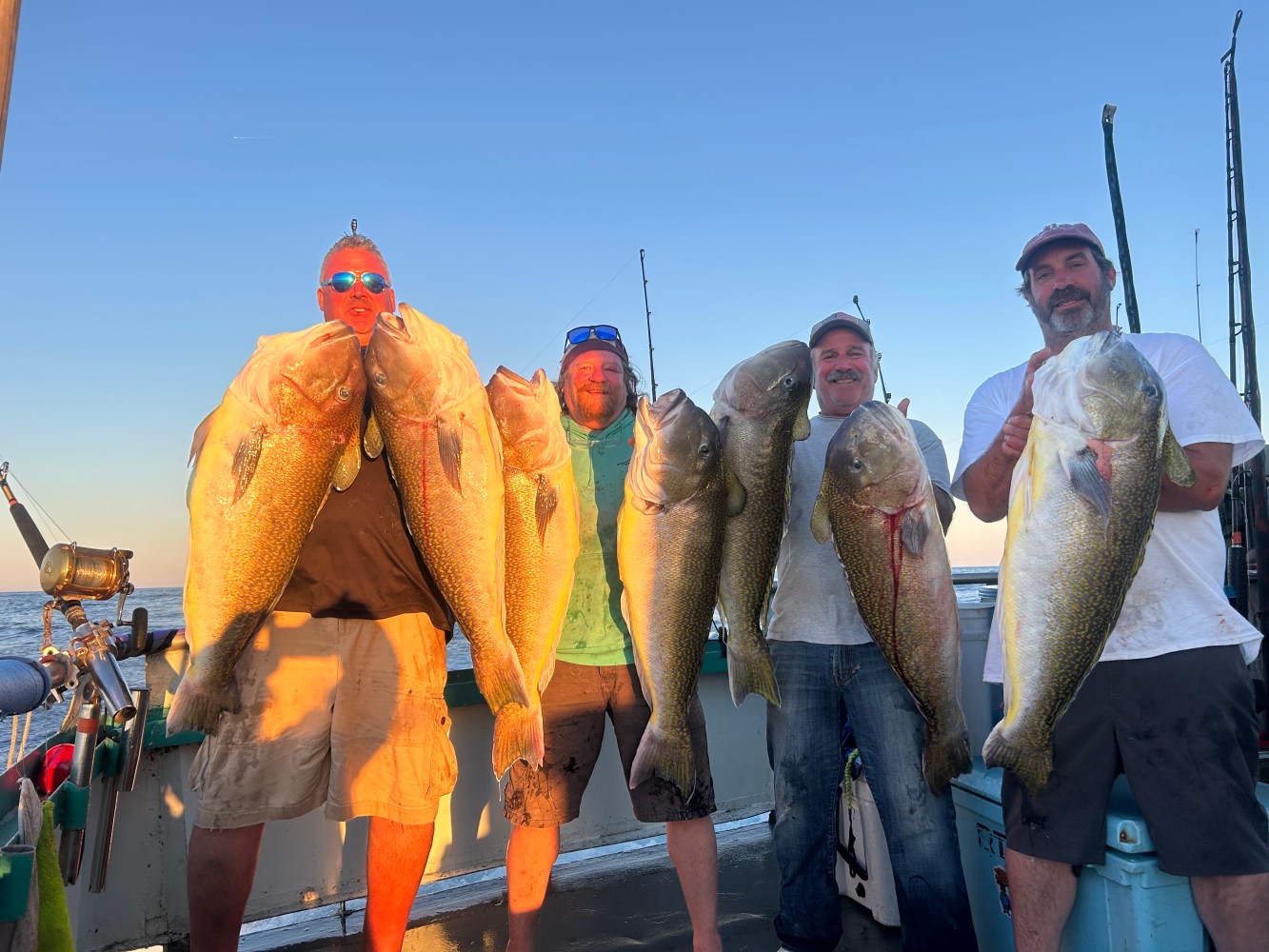Four people on a boat holding large fish during sunset.