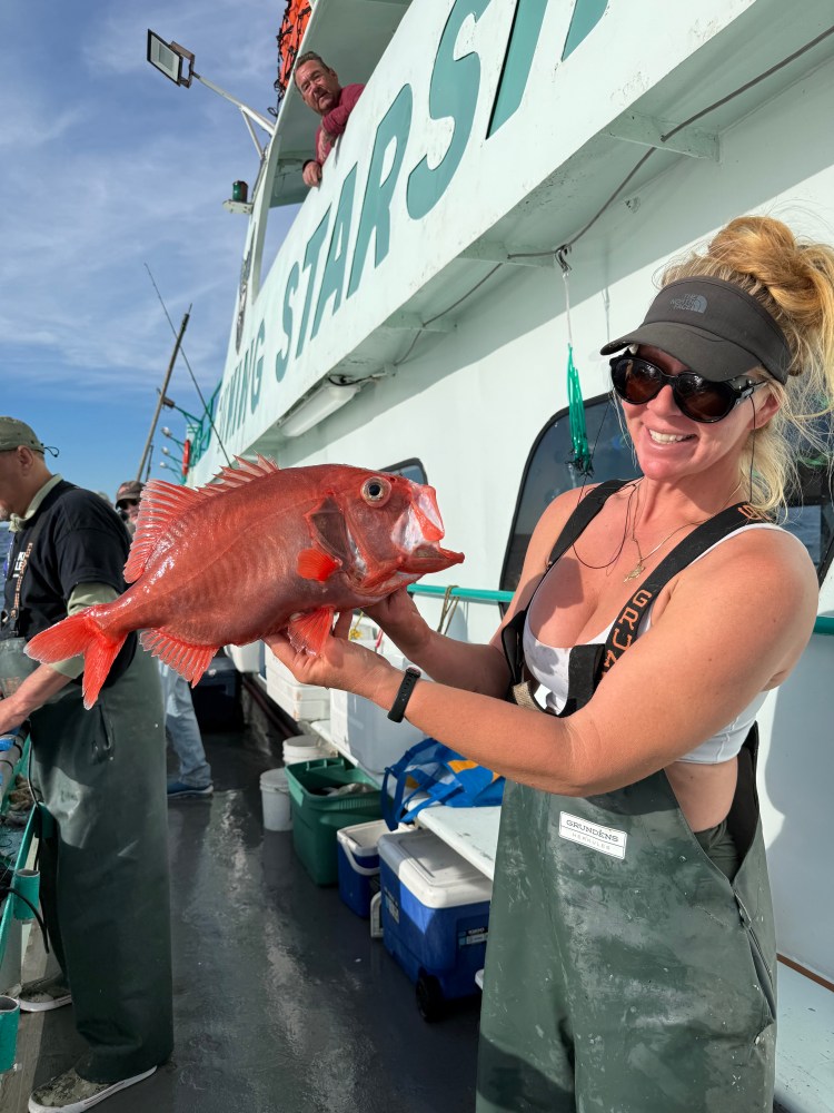 Person in fishing gear holding a large red fish on a boat.