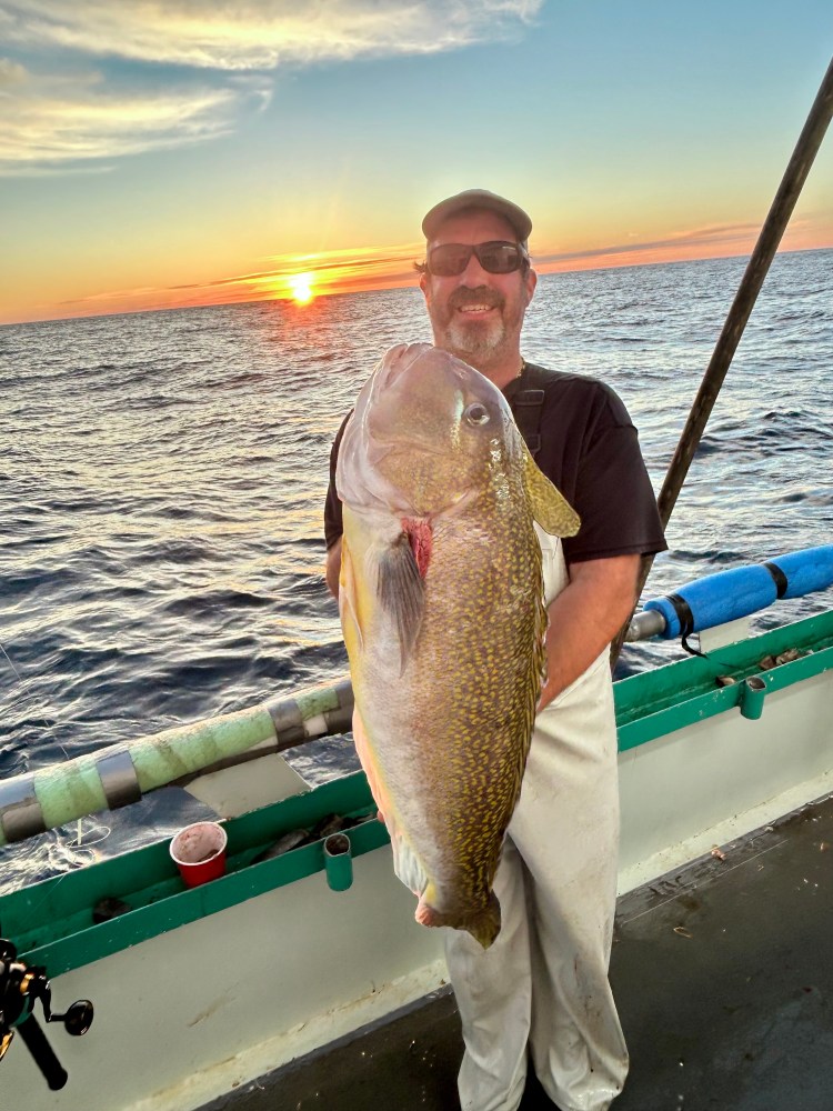 Man holding large fish on a boat at sunset.