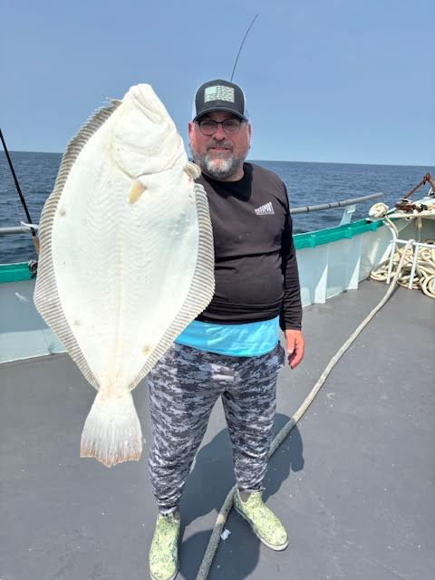 Person holding a large fish on a boat with ocean in the background.