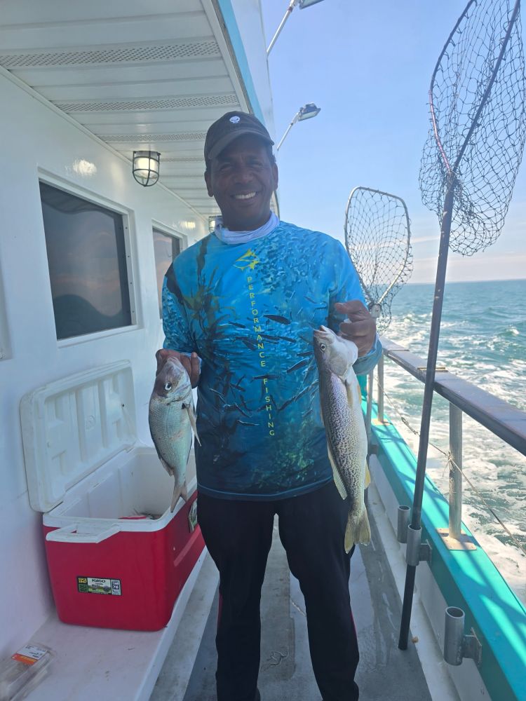 Person on a boat holding two fish near a cooler with fishing nets in the background.