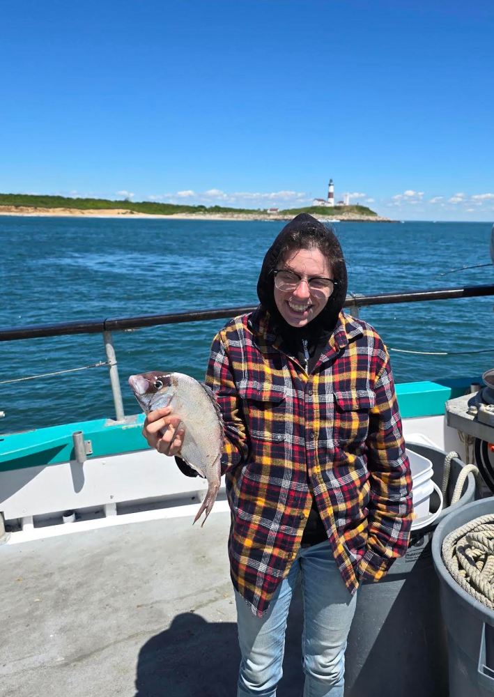 Person holding a fish on a boat near a lighthouse.