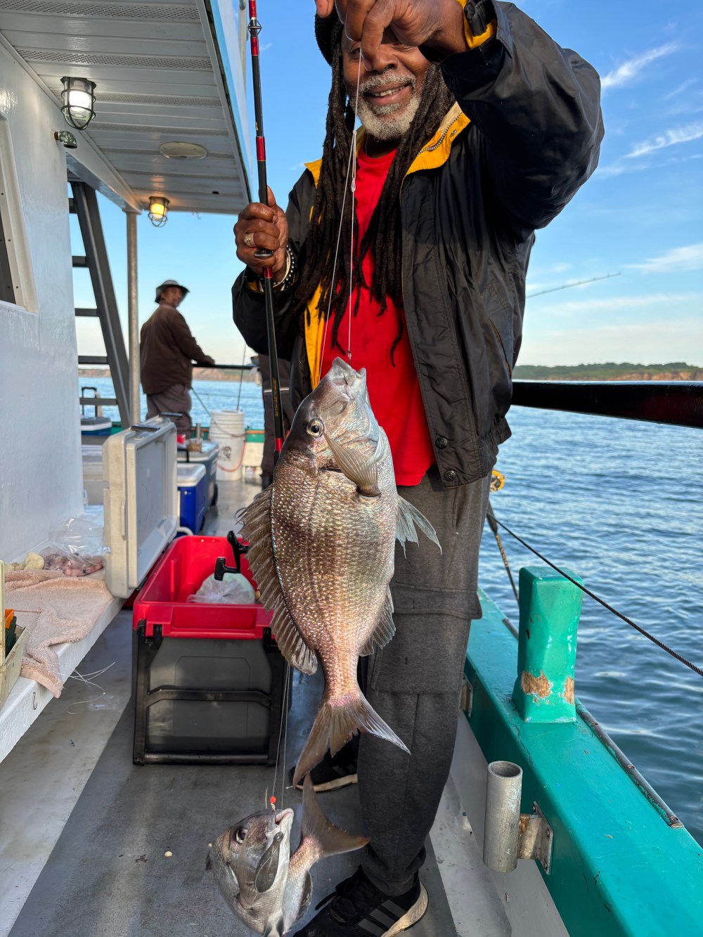 Man on boat holding two fish on a line near water's edge.